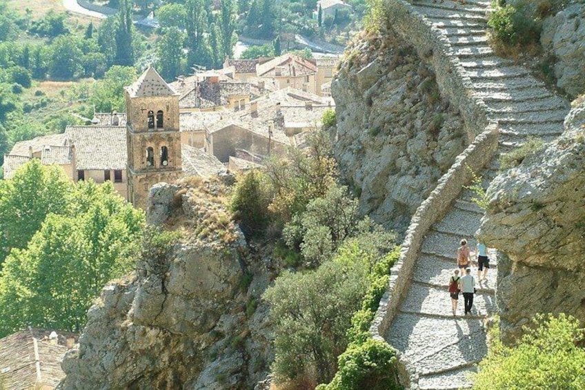 Una escalera de piedra conduce a un edificio histórico con un campanario, rodeado de vegetación y un pueblo al fondo. 3