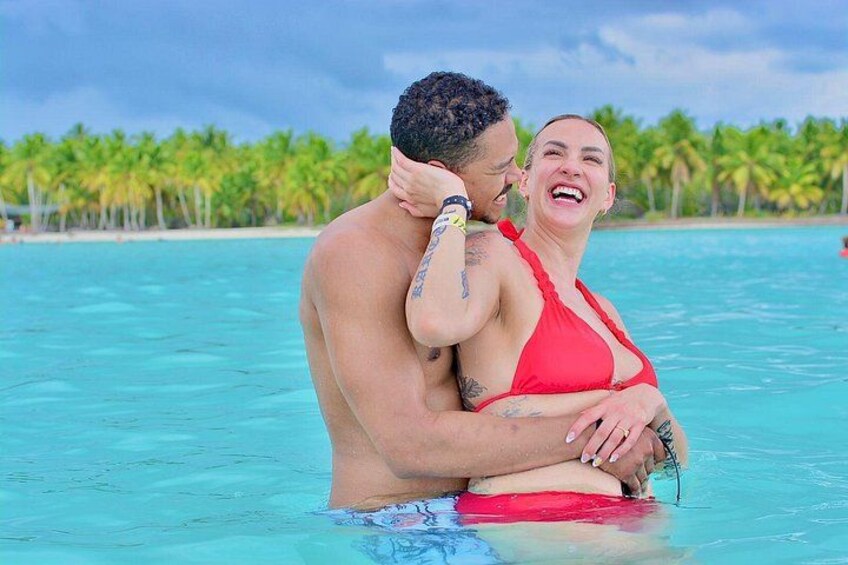 Una pareja se abraza en un océano azul cristalino, con palmeras al fondo. 5