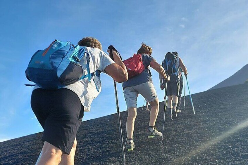 A group of hikers ascending a volcanic slope with backpacks and trekking poles. 1