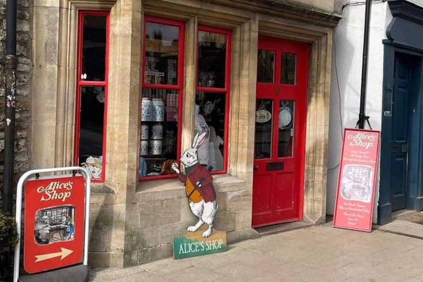 A shop with a red door and windows, a rabbit statue, and signs for 'Alice's Shop.' 3