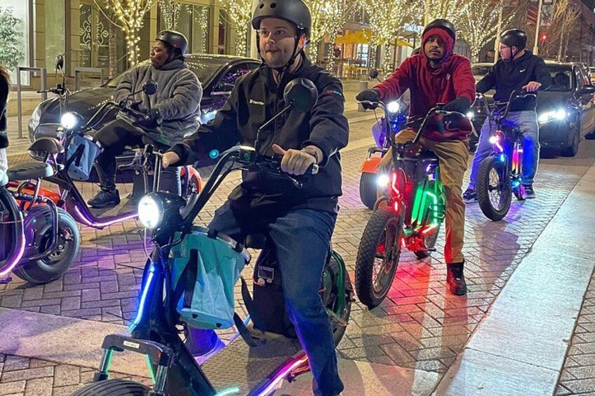 People riding electric scooters with colorful lights on a paved path. 1