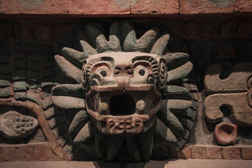 Eine Steinschnitzerei eines Gesichts mit Kopfschmuck vor einer Backsteinmauer. 3