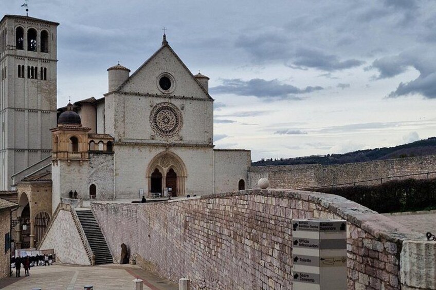 A historic church with a bell tower, a large circular window, and a stone wall with a staircase leading to the entrance. 2