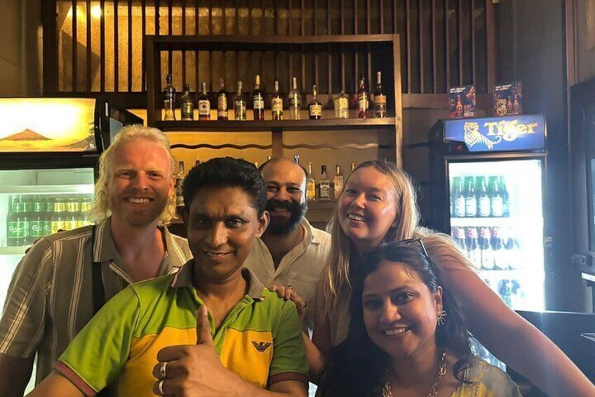 Un grupo de personas en un bar con estantes llenos de botellas y un refrigerador. 2