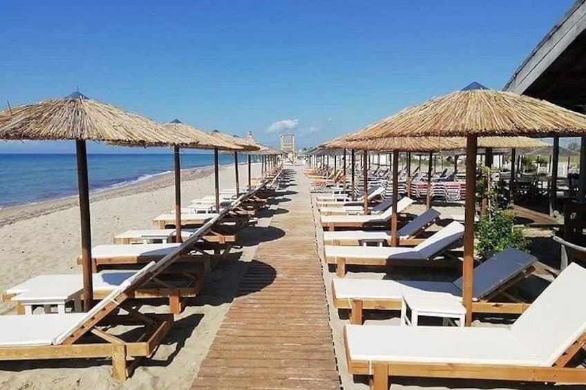 A beach with wooden lounge chairs and thatched umbrellas. 1