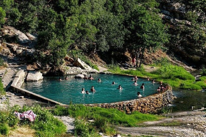 Ett naturligt badområde omgivet av grönska och ett kuperat, stenigt landskap. 1