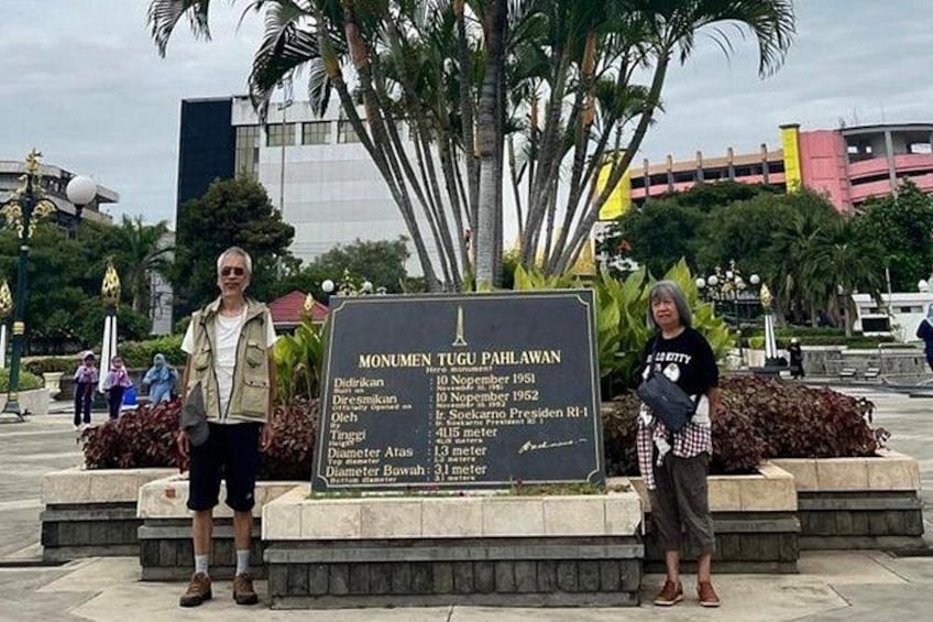 A monument with a list of names and dates, surrounded by palm trees and a modern building in the background. 5
