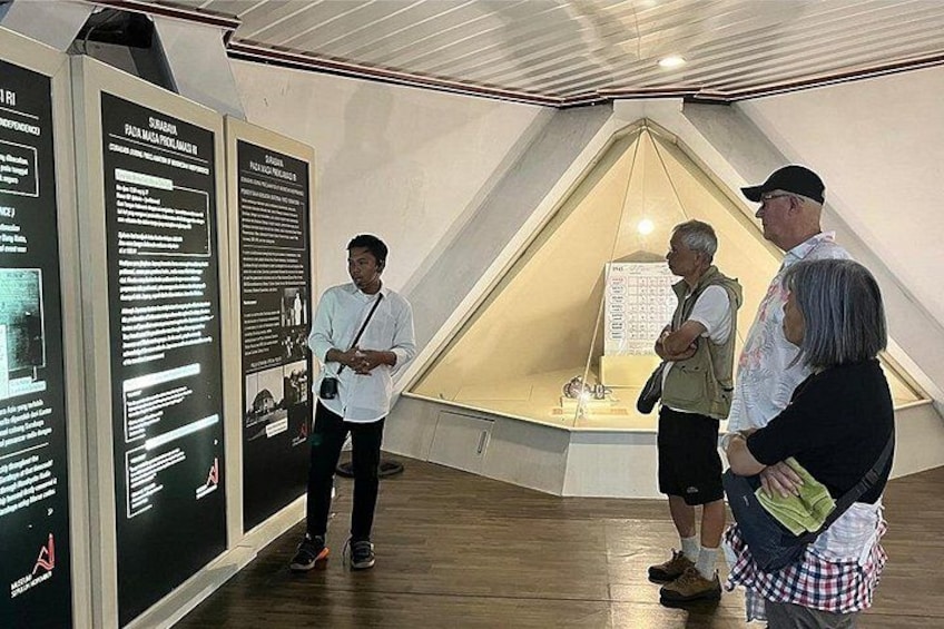 A group of people in a museum-like setting with informational displays and a triangular glass enclosure. 4