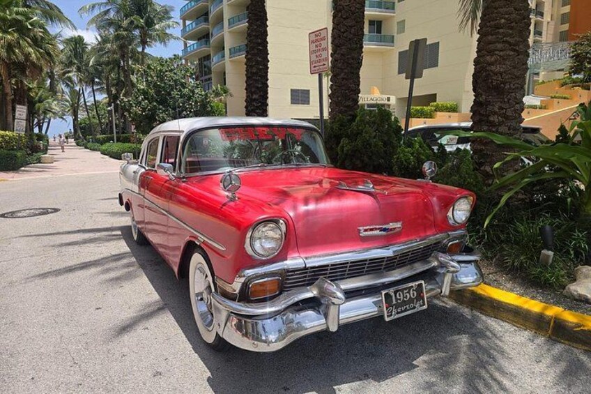 A red vintage car parked on a street with palm trees and a building in the background. 3
