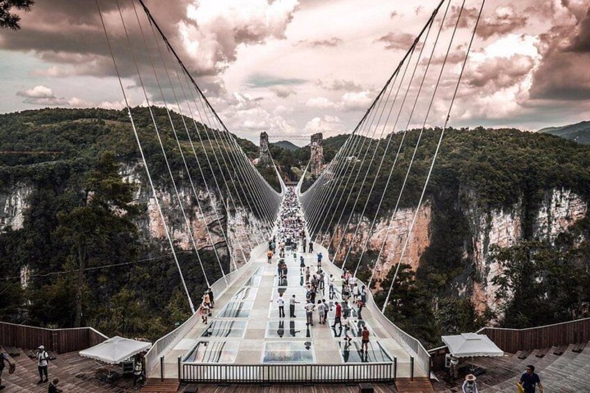 A suspension bridge with a walkway, surrounded by forested hills. 4