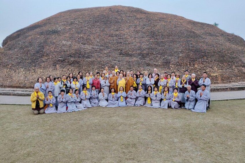 A group of people in traditional attire posing in front of a large, ancient stone structure. 4