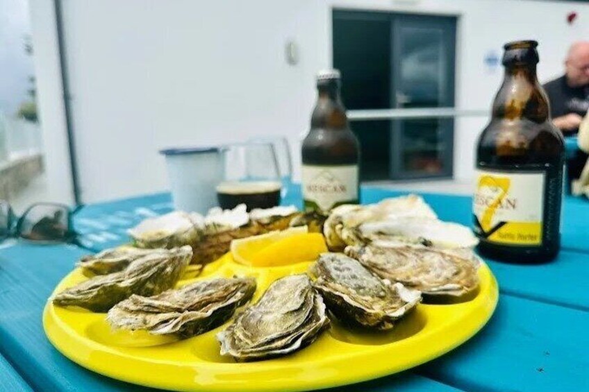 A yellow plate with oysters and two bottles of beer on a blue table. 4