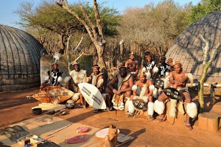 Un groupe de personnes assises à l’extérieur, avec des huttes traditionnelles en arrière-plan. 5