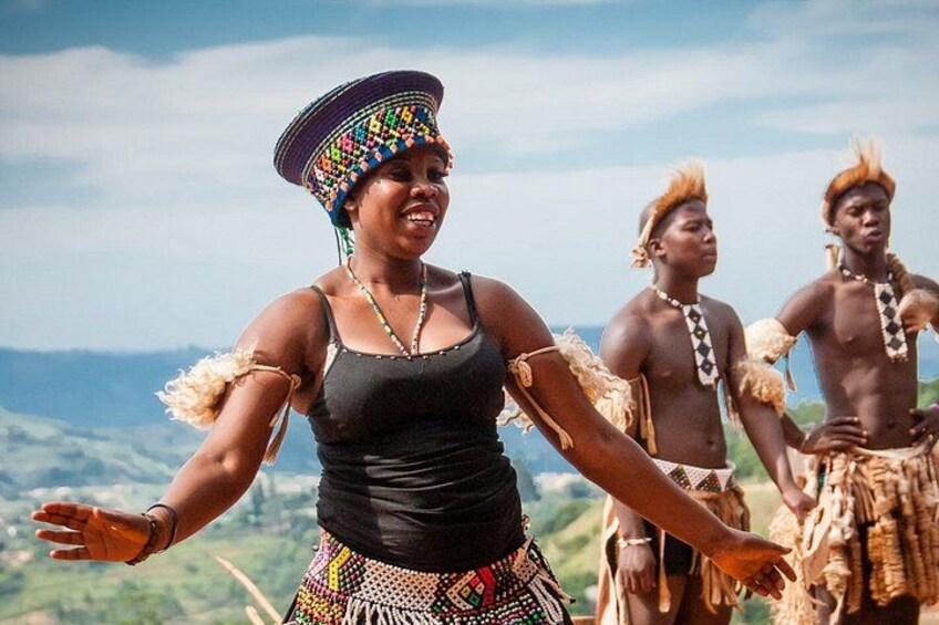 A person in traditional attire with outstretched arms, a mountainous landscape in the background, and another individual in the background. 3