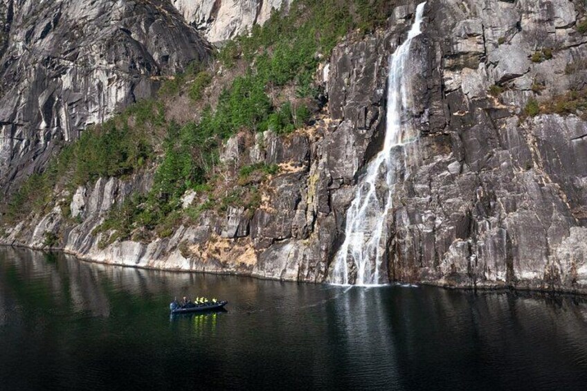 A waterfall cascading down a rocky cliff into a calm lake, with a small boat on the water. 3