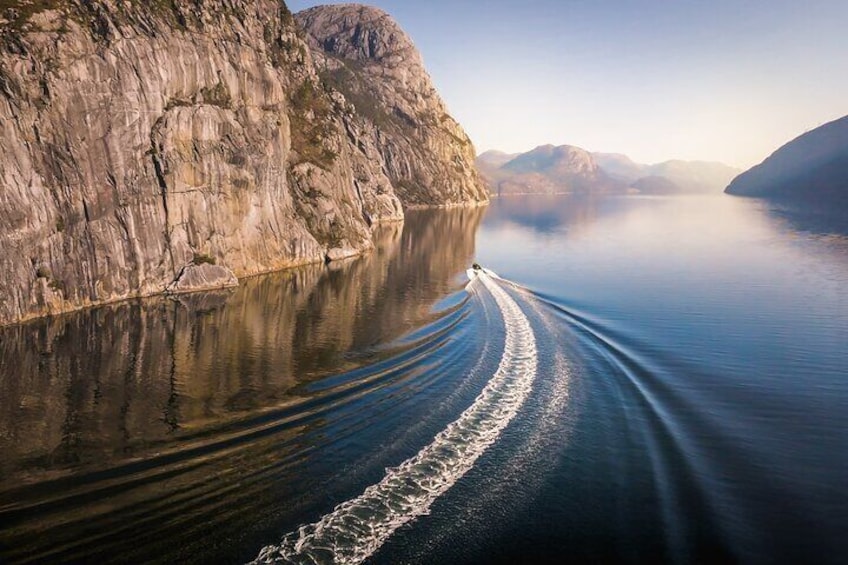 A boat creating a wake on a calm lake surrounded by rocky cliffs. 5
