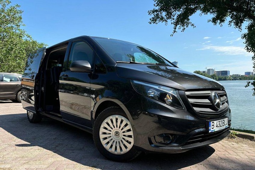 Un Mercedes-Benz negro con patente visible, estacionado junto a un cuerpo de agua con árboles al fondo. 2