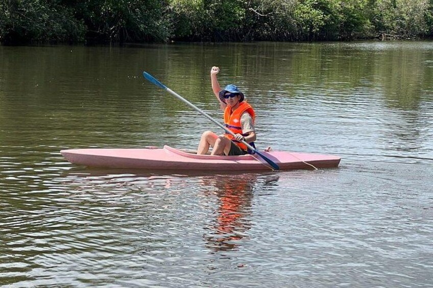 Una persona en un kayak rosa sobre aguas tranquilas, vestida con un chaleco salvavidas naranja y un sombrero azul. 2