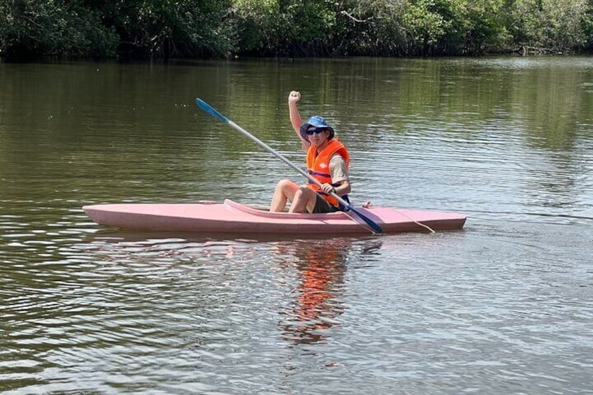 Una persona en kayak rosa en un río tranquilo, usando chaleco salvavidas naranja y gorra azul. 4