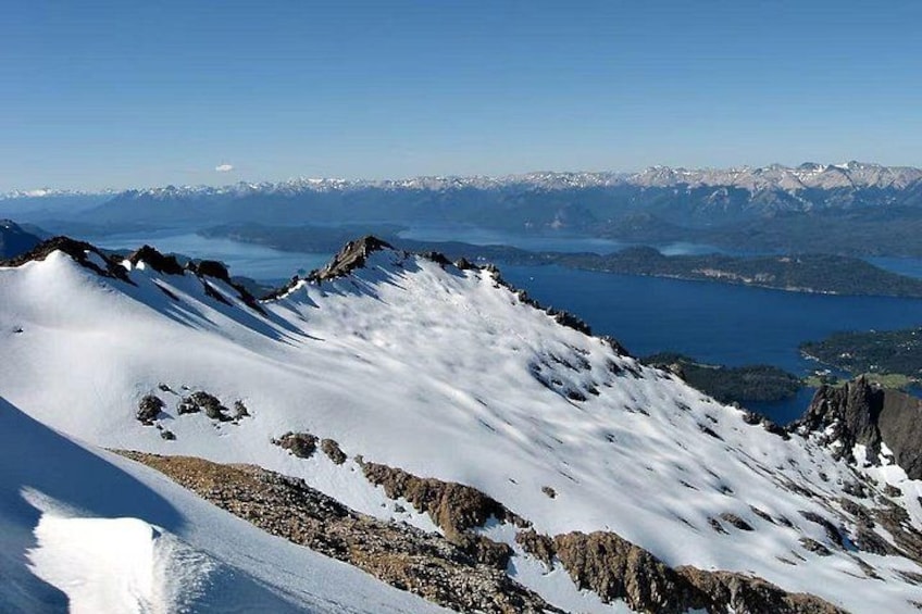 A snow-covered mountain ridge with a lake and distant mountains in the background. 2