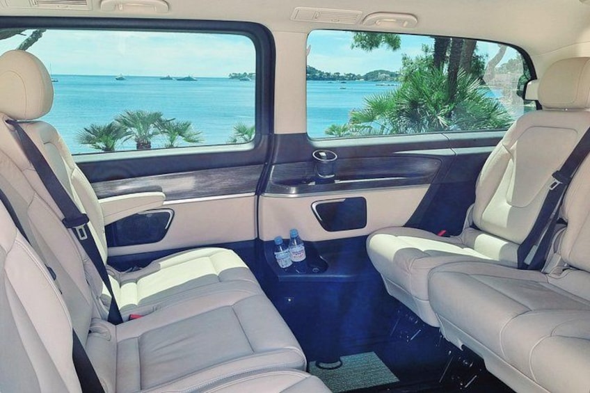 Een auto-interieur met twee beige stoelen, een middenconsole en uitzicht op zee door de ramen. 3