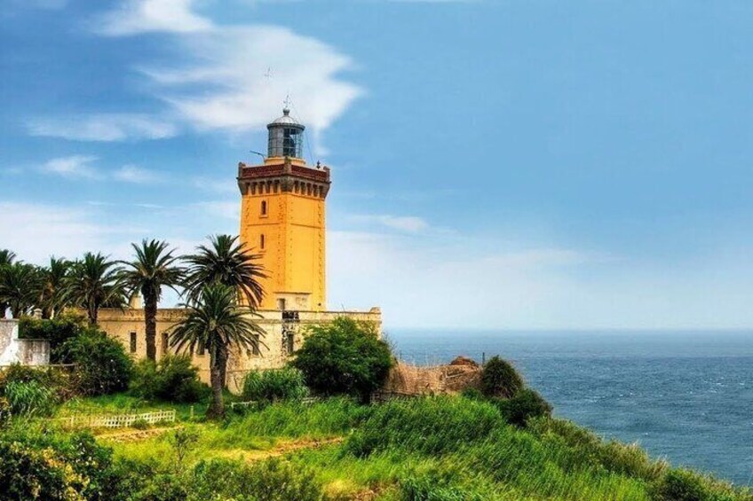 Un faro costiero con una torre gialla, palme e vista sul mare. 1