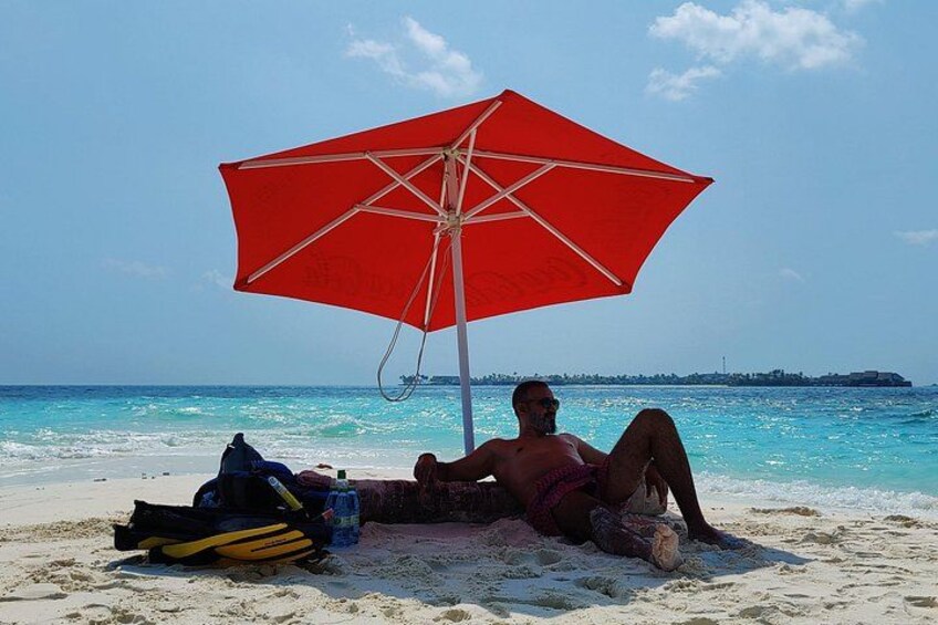 En strand med en rød parasol, en person, der ligger i sandet, og en klar blå himmel. 4