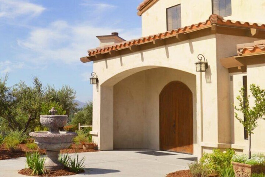 A stucco building with a tiled roof, a wooden door, and a stone fountain in the foreground. 3
