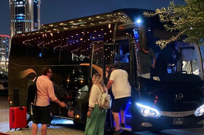 En bus med folk, der stiger af og på, en rød kuffert, og et bybillede om natten. 2