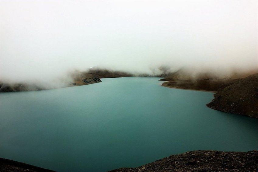 A turquoise lake surrounded by rocky terrain and enveloped in mist. 2