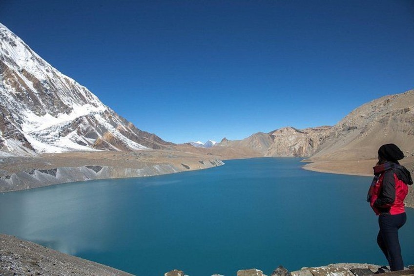 A person standing on a rocky outcrop overlooking a turquoise lake surrounded by mountains. 3