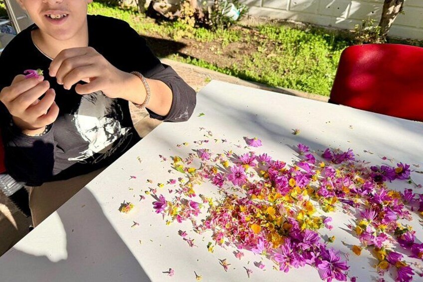 Una persona sentada a una mesa con mantel blanco, rodeada de flores dispersas. 5