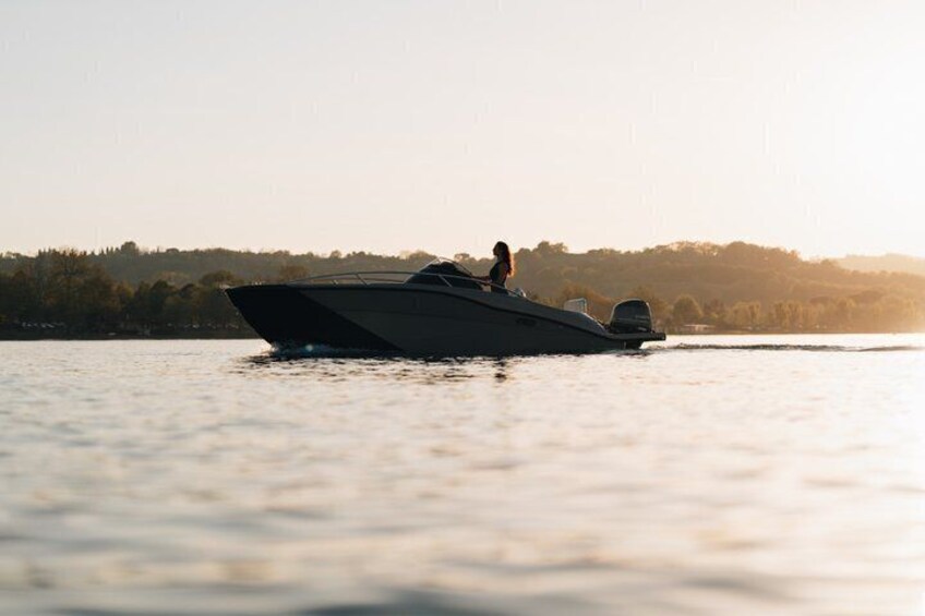 A speedboat on calm water with a person on board, a shoreline with trees in the background, and a clear sky. 3