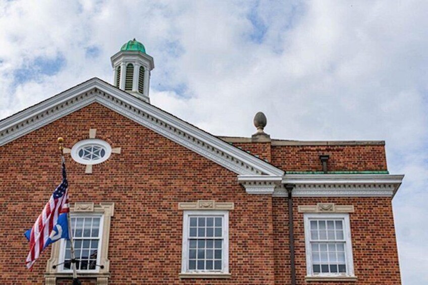 A brick building with a green roof, a flagpole with an American flag, and a circular window on the facade. 2