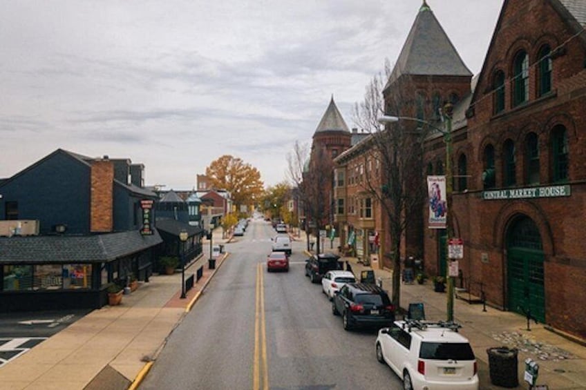 A street lined with brick buildings, a central market house, and parked cars. 4