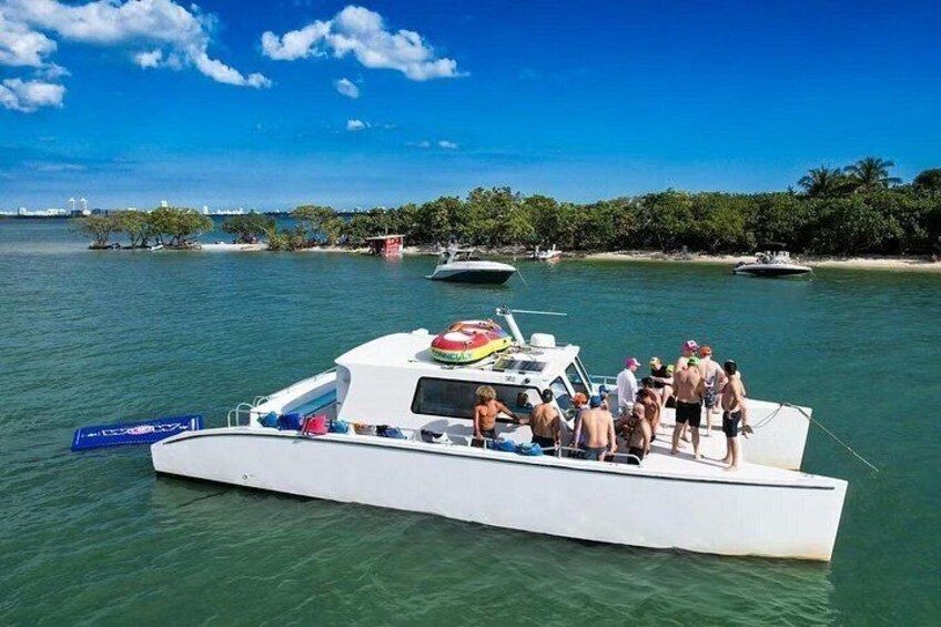 Ein weißes Boot mit Personen am Ufer, wo Bäume und andere Boote liegen. 1
