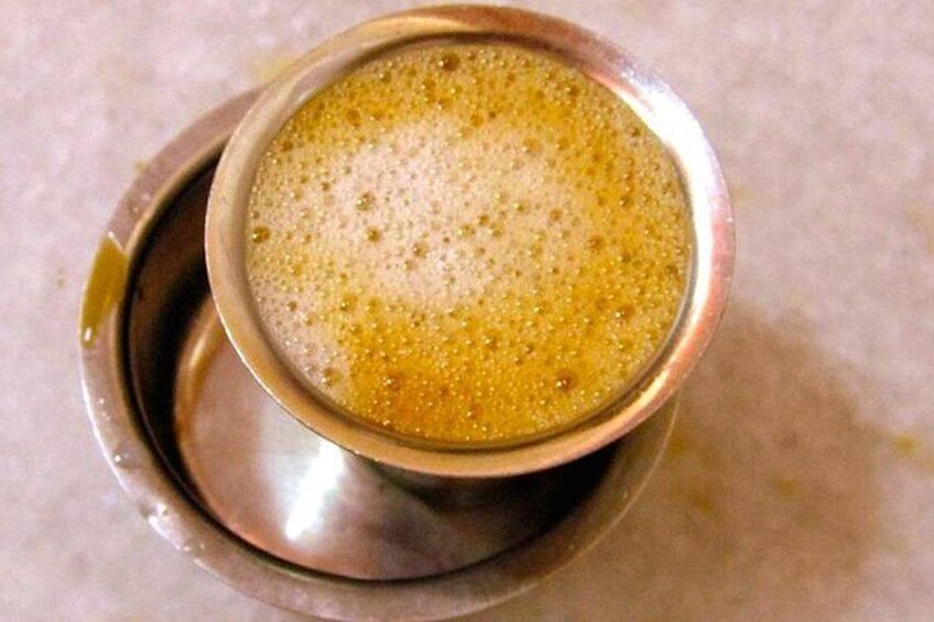 A metal cup with a frothy beverage, possibly coffee or tea, on a metal saucer. 2