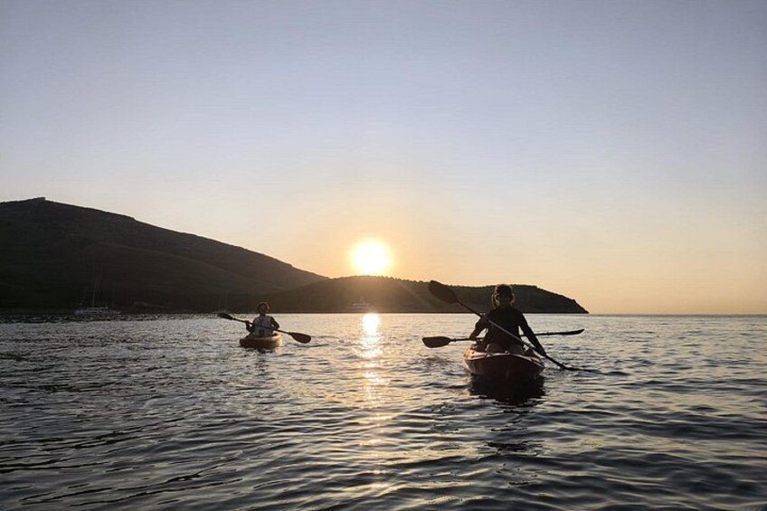 Deux personnes pratiquant le kayak sur un lac paisible au coucher du soleil, avec une montagne en arrière-plan. 3