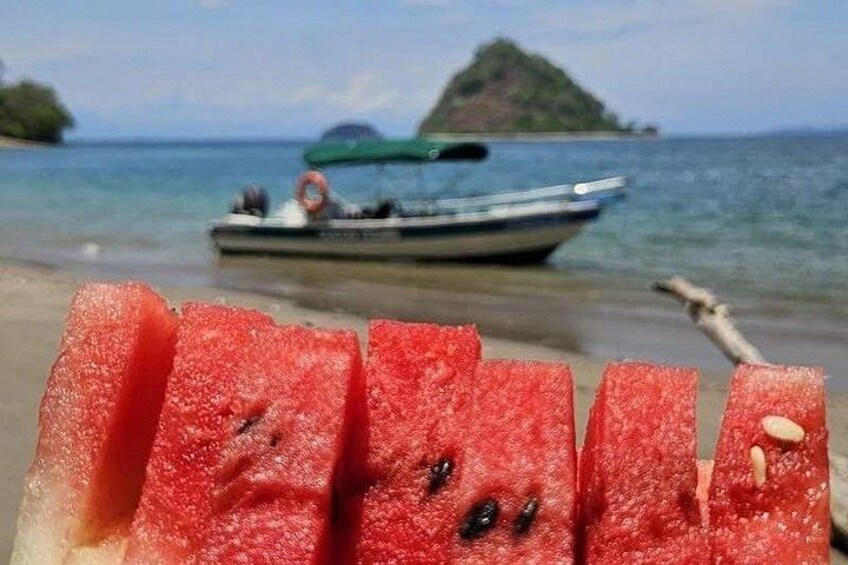 A beach with a boat in the background and a watermelon in the foreground. 3