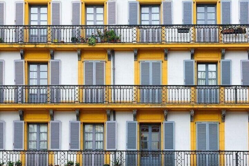 A multi-story building with yellow and white facades, grey shutters, and black railings. 2