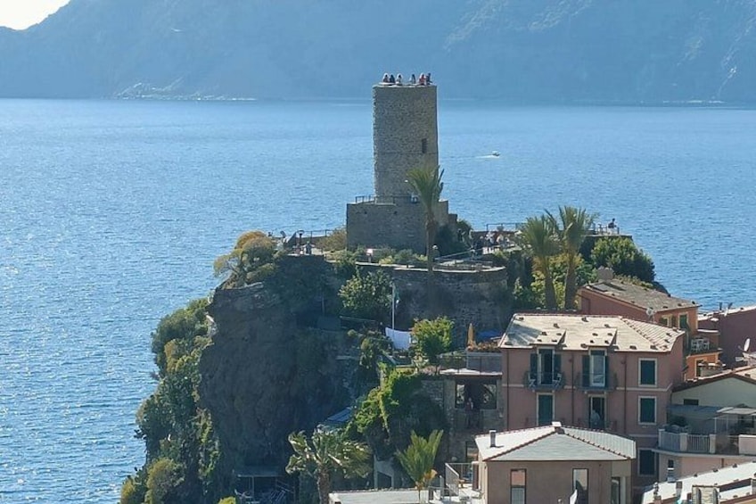 A coastal town with a prominent tower on a cliff, buildings, and a clear blue sea. 2