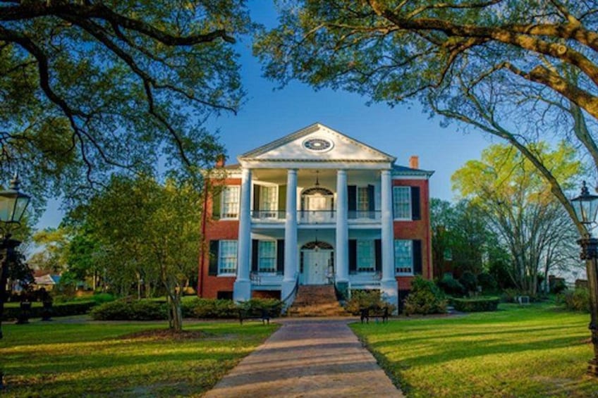 A large, two-story building with a central entrance, surrounded by well-maintained lawns and trees. 2