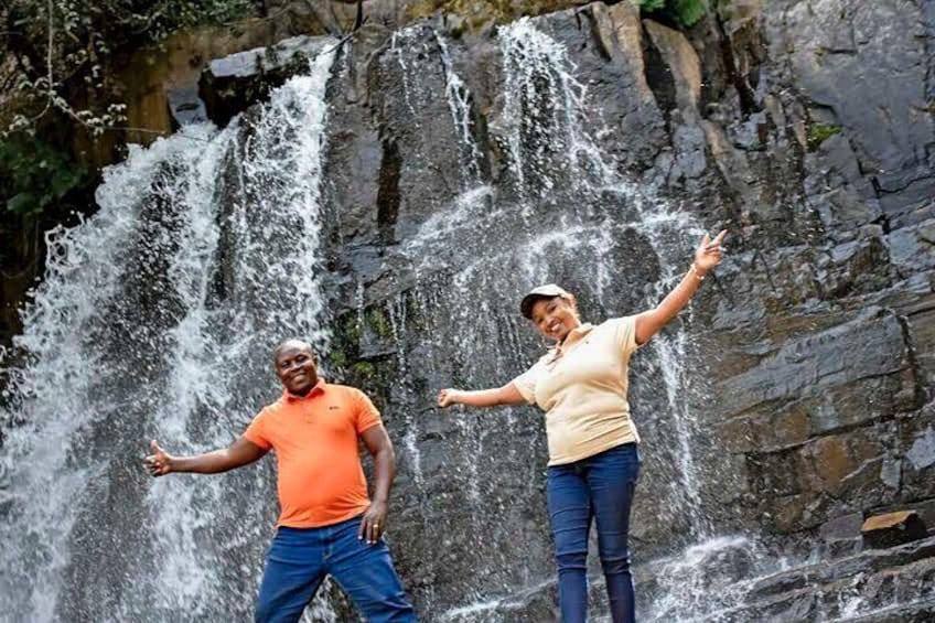 Twee personen staan voor een waterval, met water dat over een rotsachtige klif stroomt. 2