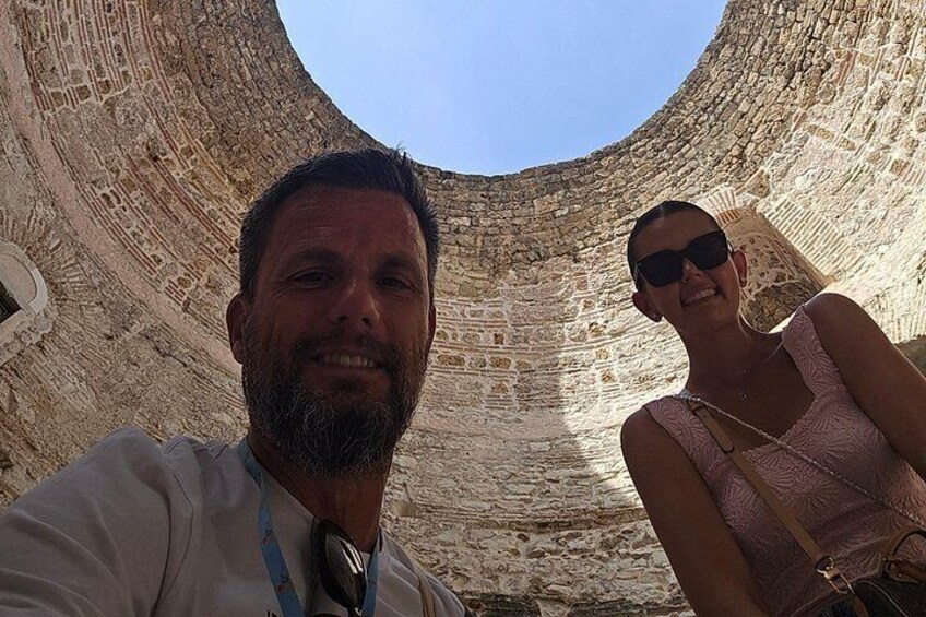 Un homme et une femme se trouvent à l’intérieur d’une grande structure circulaire en pierre, et on peut voir un ciel dégagé par le sommet. 4