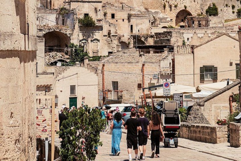 Una strada in una città storica con edifici antichi, un camion parcheggiato e persone che passeggiano. 2