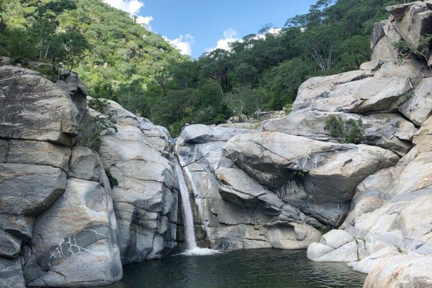 A waterfall cascading over large rocks into a pool, surrounded by dense green forest. 1