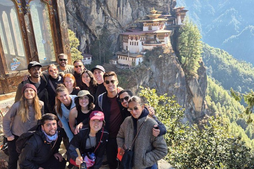 Un grupo de personas posando frente a un paisaje montañoso con un monasterio. 5