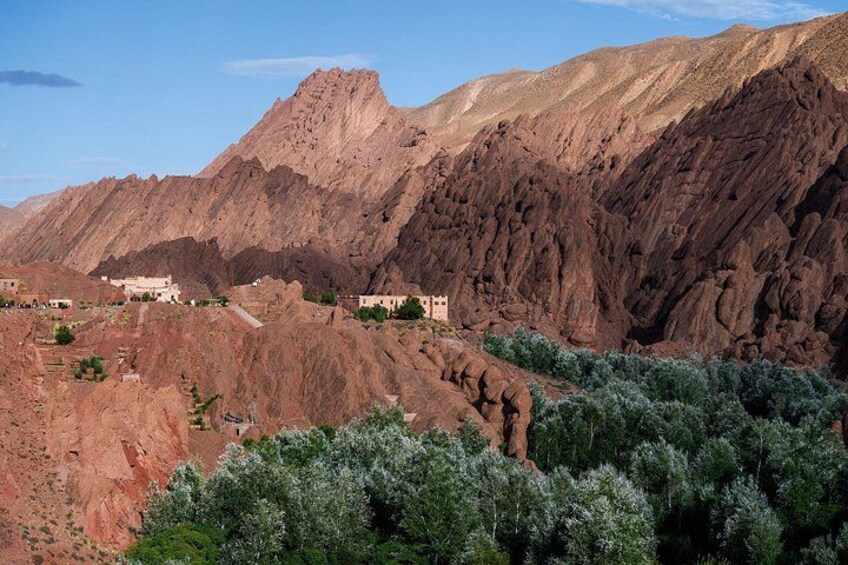 A rugged mountainous landscape with sparse vegetation, a small settlement, and a prominent rocky peak. 2