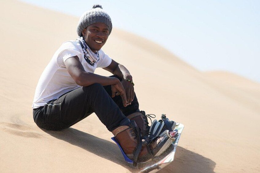 A person sitting on a sand dune with a backpack and a pair of shoes. 4