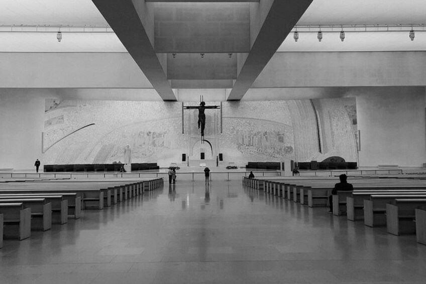 An empty church interior with rows of pews, a large cross, and a mural on the wall. 5